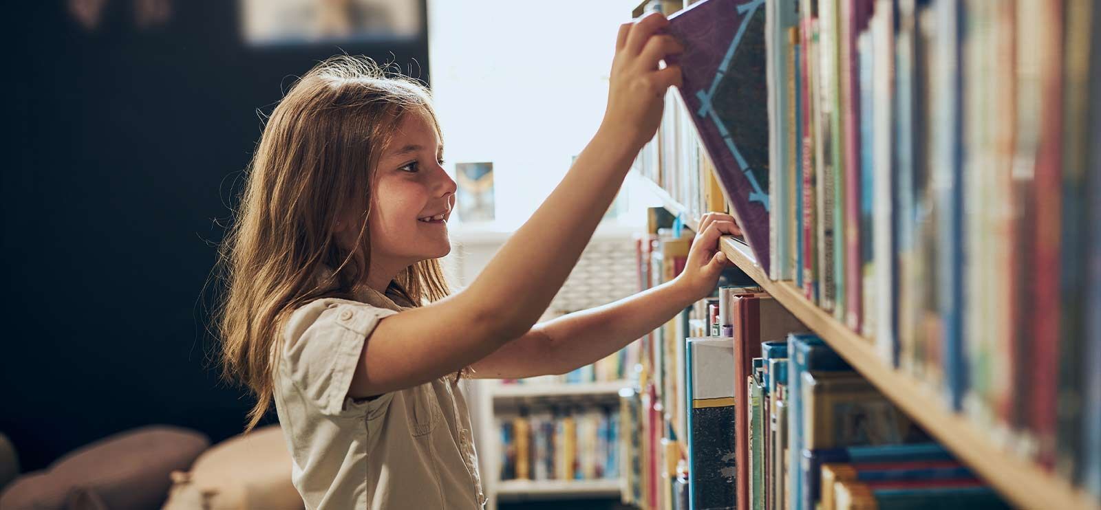 Jente med brunt hår som plukker en bok ut av en bokhylle. Foto Przemek Klos