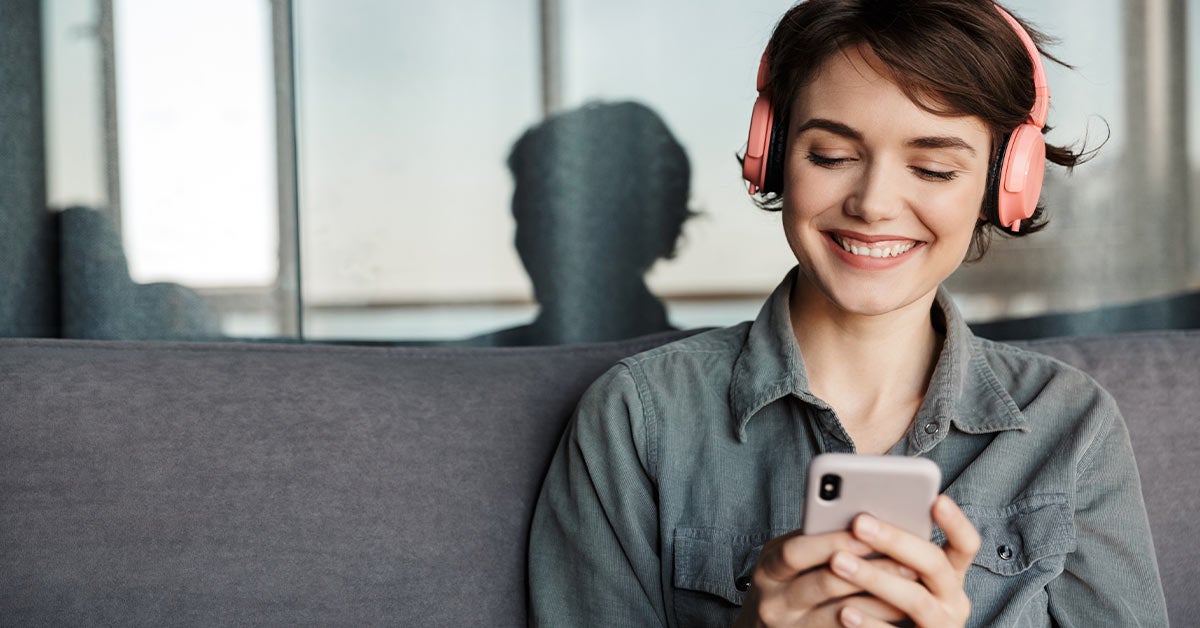 Dame som smiler mens hun ser på mobilen. Hun har på et headset.