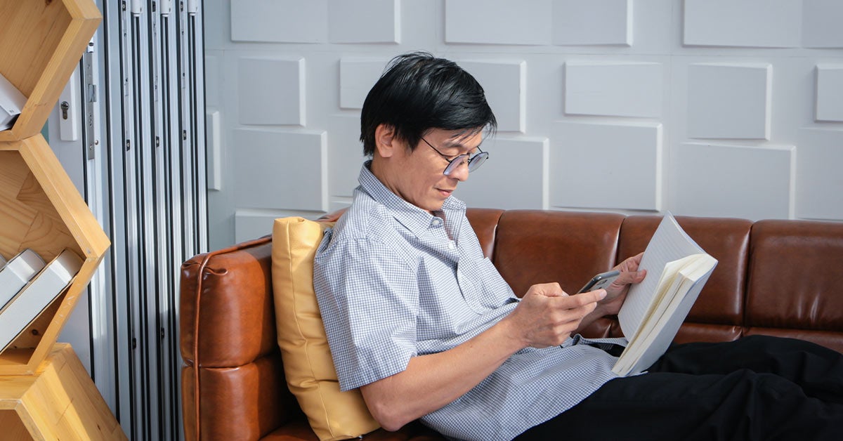 Mann sitter i en sofa med mobil og en bok