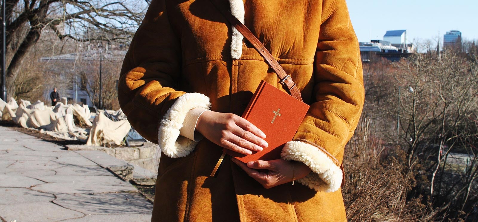 Bibelen 2024. Kvinne holder en rød bibel i parken.