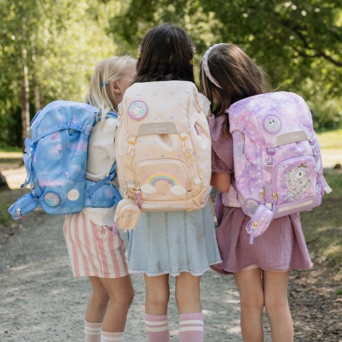 Tre jenter bærer sekk med ryggen til kameraet