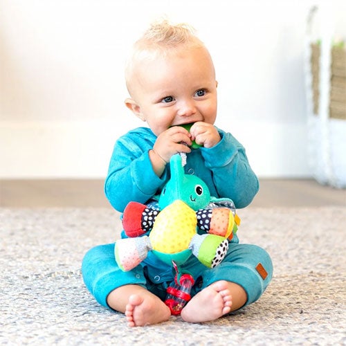 Baby i blå sparkedress som biter på rangle