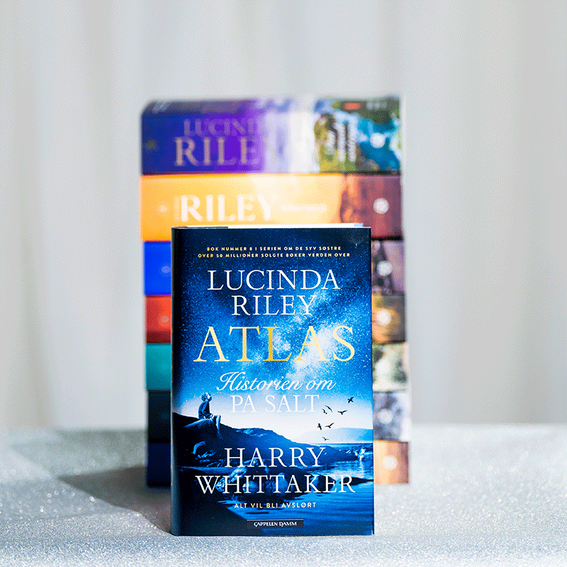 I bakgrunnen ligger en bunke med alle bøkene i serien De Syv Søstre av Lucinda Riley. I front er den åttende og siste boka i serien - Atlas.